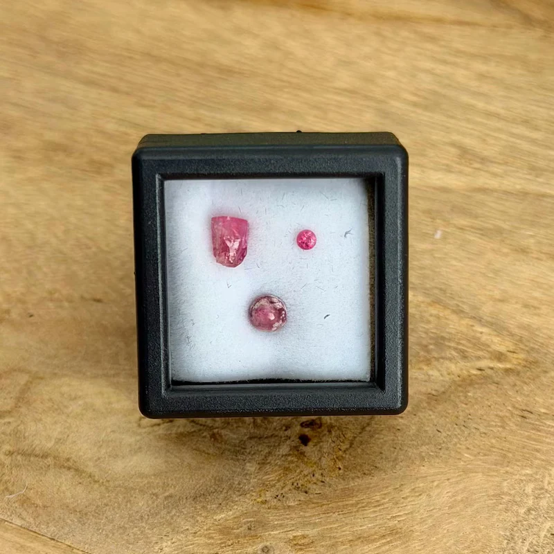 Three small red and pink beryl pieces in a black collector display box